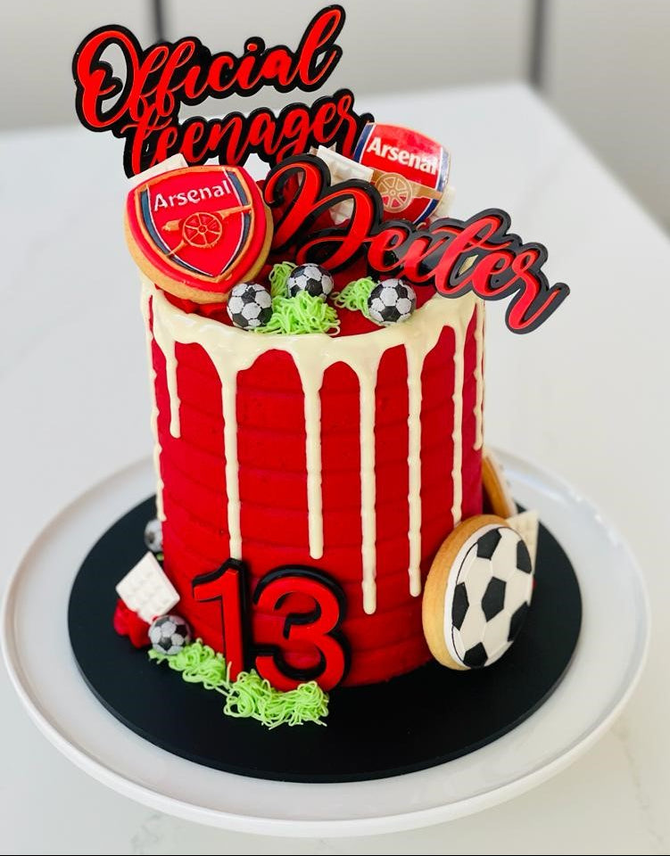 Red birthday cake with Arsenal-themed decorations on a white surface