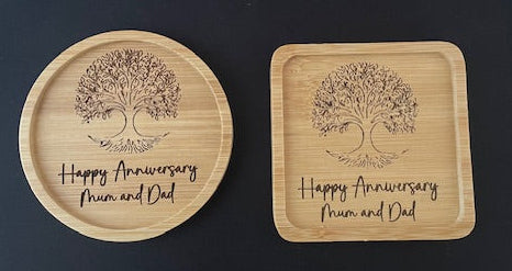 Two wooden coasters with engraved tree design and text on a black surface.