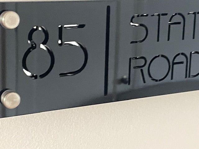 Metallic address plaque with numbers '85' and text 'STATE ROAD' on a reflective surface.