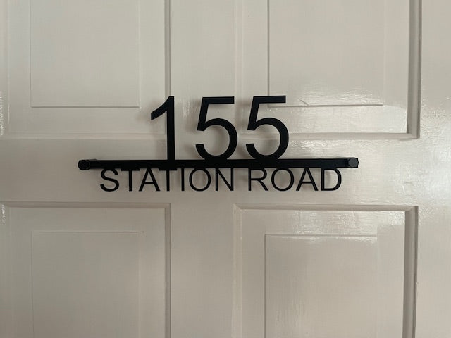 Black house number sign with '155 Station Road' on a white door