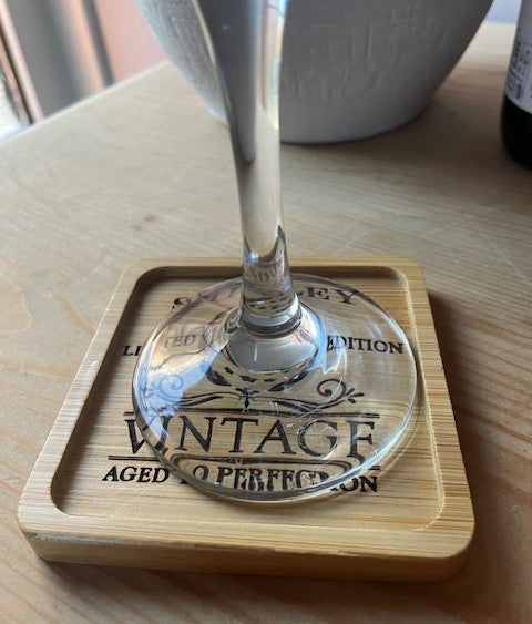 Glass with a wooden coaster featuring 'Vintage Aged to Perfection' text on a wooden surface.