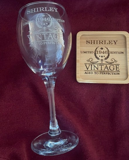 Wine glass and wooden coaster with 'Shirley' branding on a red fabric background