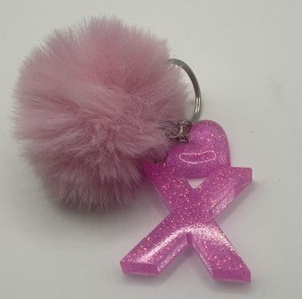 A pink glittery acrylic ribbon keychain charm with a fluffy pink pom-pom and a silver metal key ring, shown on a plain white background.