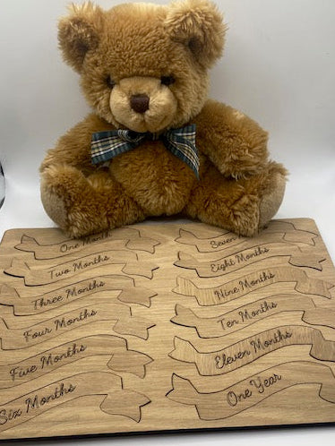 Brown teddy bear with a plaid bow tie next to a wooden board with engraved names.