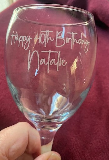 Clear glass wine glass with 'Happy 10th Birthday Natalie' text held against a red background.