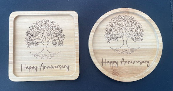 Two wooden coasters with tree design and 'Happy Anniversary' text on a blue surface.
