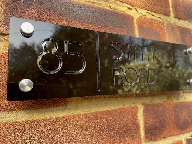 Black rectangular sign with '85 Station Road' on a brick wall