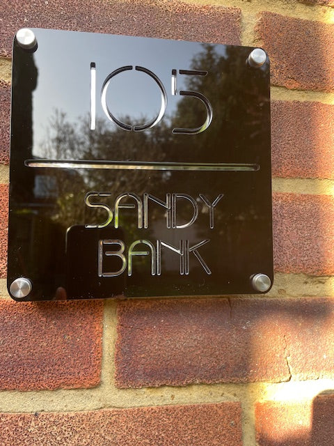 Metal sign with '105 Sandy Bank' on a brick wall