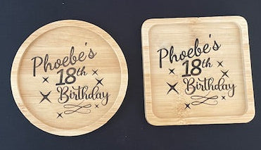 Two wooden coasters with 'Phoebe's 18th Birthday' text on a black surface, branded 'TECKNET'.