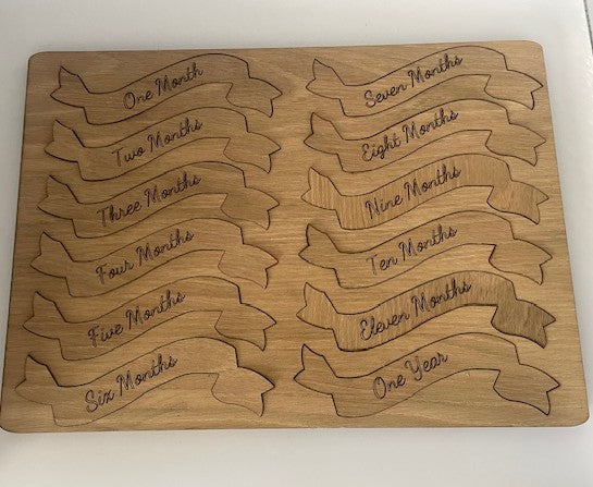Wooden board with engraved milestone banners for baby growth tracking.