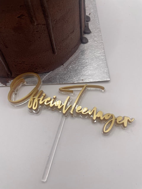 Gold 'Official Teenager' cake topper on a chocolate cake with silver sides.