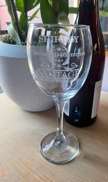 Wine glass with engraved text on a wooden surface next to a bottle