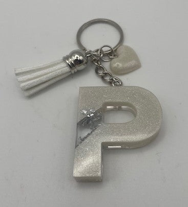 A silver glitter letter 'P' keychain with a white faux-leather tassel, a silver key ring, and a small white heart charm on a plain light background.