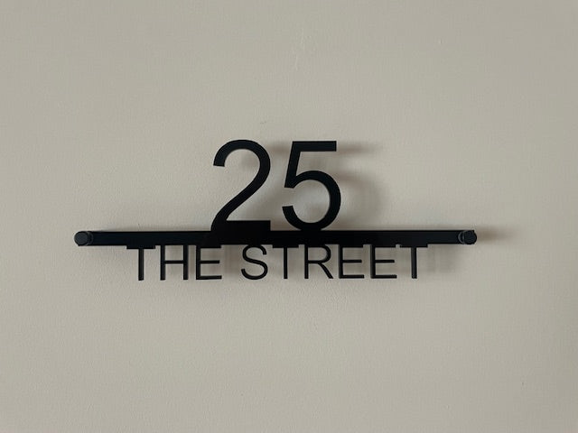 Black metal address sign with '25 THE STREET' on a beige background