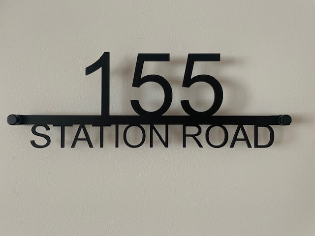 Black house number sign with '155 Station Road' on a beige wall