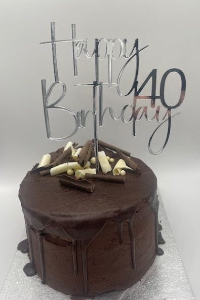 Chocolate cake with white chocolate pieces and a 'Happy Birthday' topper on a white background