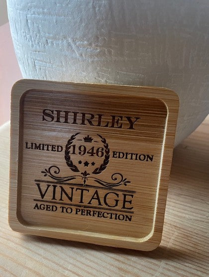Wooden coaster with engraved text 'SHIRLEY LIMITED 1946 EDITION VINTAGE AGED TO PERFECTION' on a wooden surface.