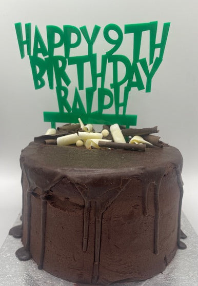 Chocolate birthday cake with 'Happy 9th Birthday Ralph' green topper on a white background