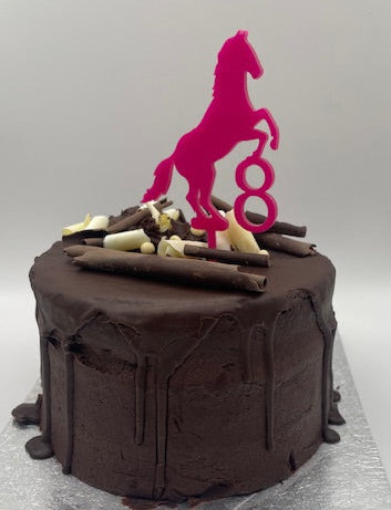 Chocolate cake with white chocolate pieces on a silver cake board, pink horse logo in the background.