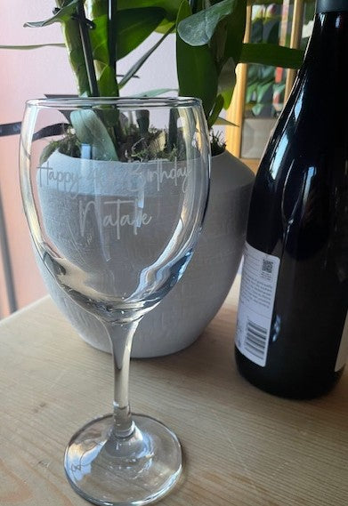 Wine glass with engraved text next to a bottle on a table
