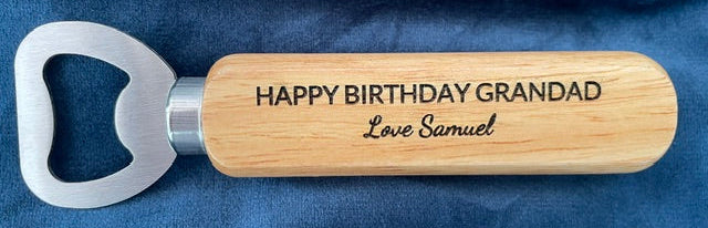 Wooden bottle opener with engraved text on a blue fabric background