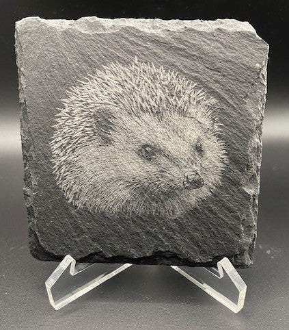 Slate tile with a engraved hedgehog design on a stand against a black background
